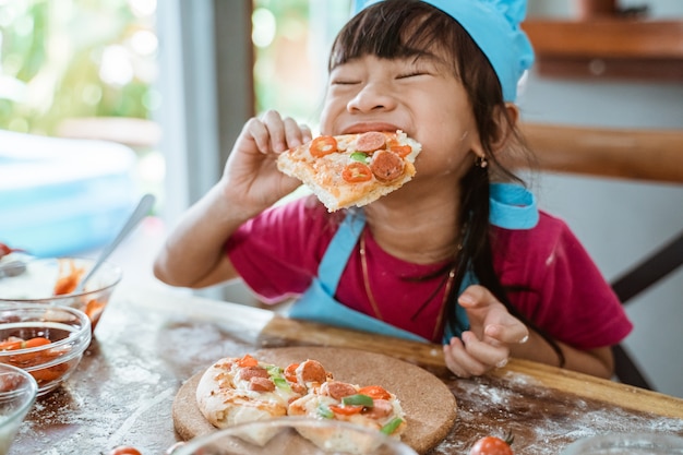 Ragazza che mangia pizza sul tavolo in cucina