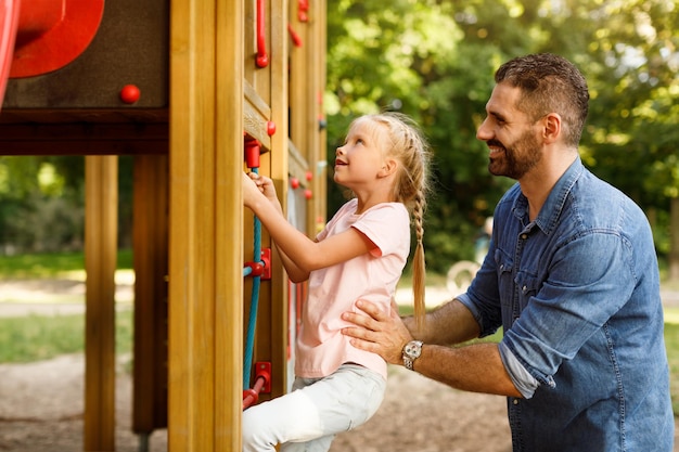 Ragazza che passa il tempo sul parco giochi padre che aiuta la figlia a salire le scale che si godono il tempo insieme in