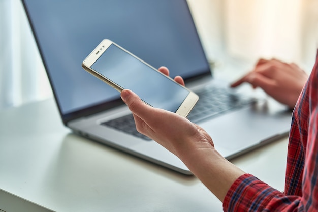 Ragazza che per mezzo di uno smartphone e di un computer portatile