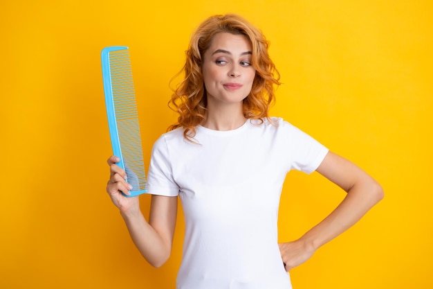 Ragazza che pettina i capelli Donna rossa con un pettine isolato su sfondo giallo