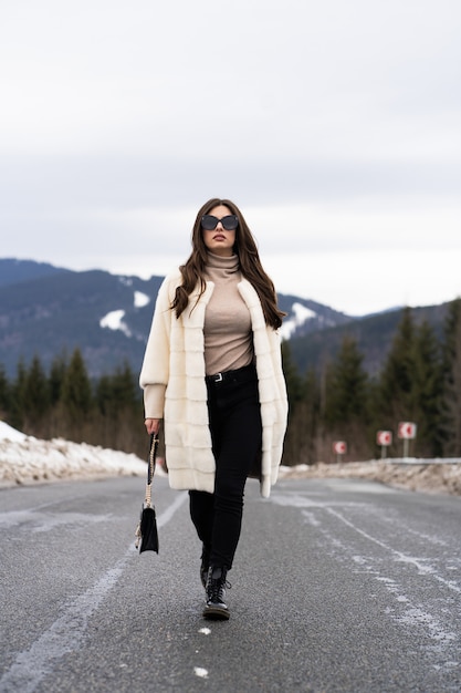 Ragazza che posa sulla strada sul bosco invernale.