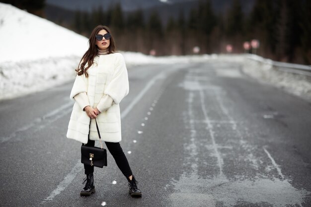 Ragazza che posa sulla strada sul bosco invernale.