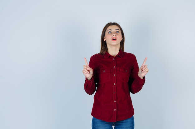 ragazza che punta e alza lo sguardo in camicetta bordeaux e sembra sorpresa.