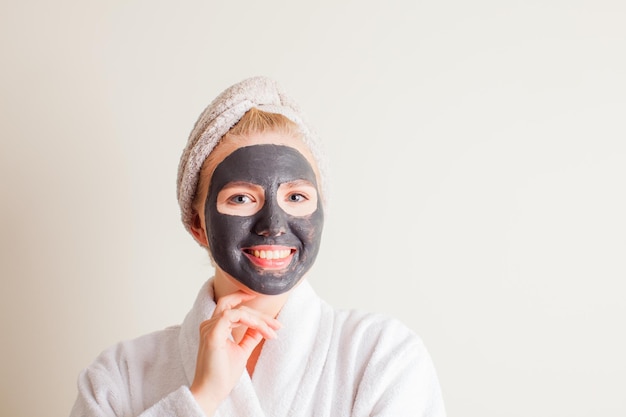 Ragazza che ride con un asciugamano in testa usando una maschera nera sul viso su sfondo bianco