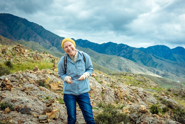 Ragazza che ride con un cellulare in mano con paesaggio montano.