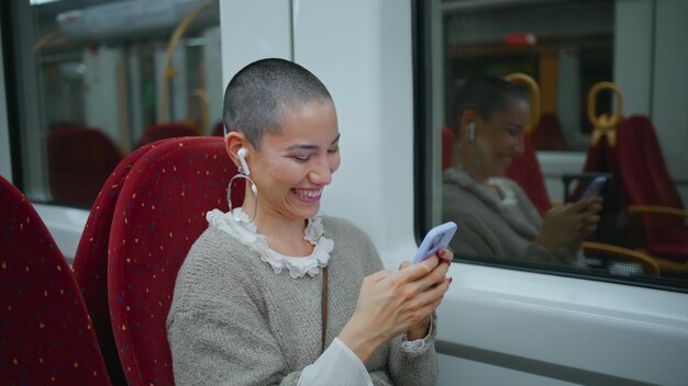 Ragazza che ride, legge un messaggio sul cellulare, viaggia in un treno moderno.