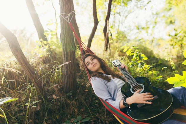 ragazza che riposa nel parco con una chitarra su un'amaca