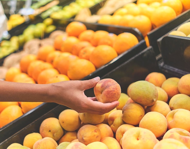 Ragazza che sceglie Peach in un negozio di alimentari Concetto di cibo sano