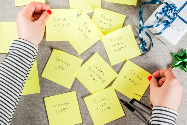 Ragazza che scrive risoluzioni di nuovi anni mani in foto Tavolo in pietra grigia con note adesive colorate con risoluzioni e penna di Capodanno popolari