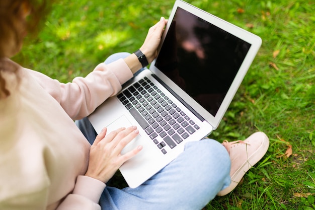 Ragazza che scrive su un computer portatile con una disposizione mentre sedendosi sull'erba nel parco