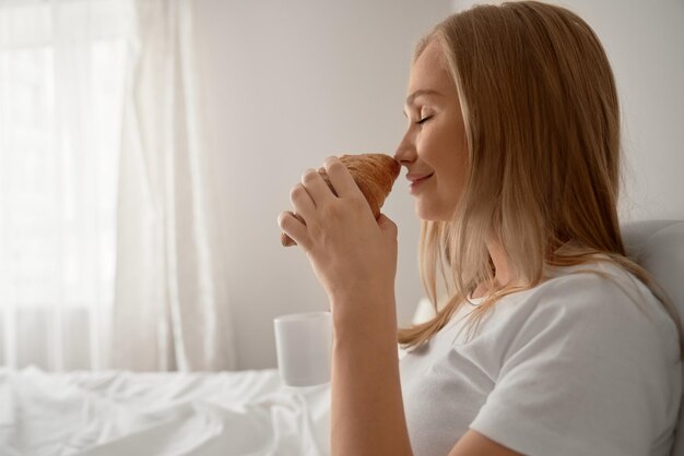 Ragazza che sente l'odore del croissant a letto