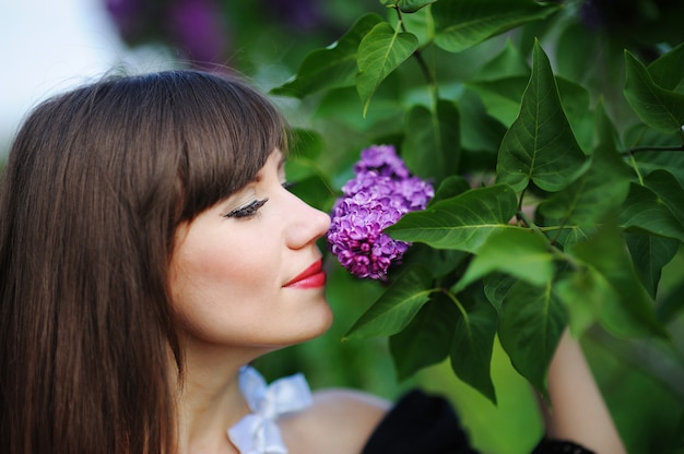 Ragazza che sente l'odore di un lillà porpora in primavera nel parco