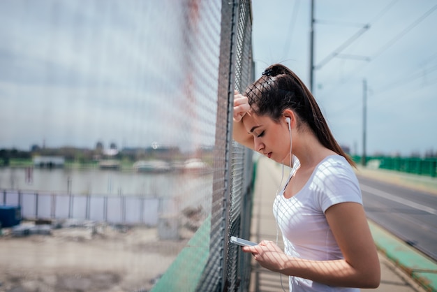 Ragazza che si appoggia sulla rete fissa che ascolta la musica sul telefono.