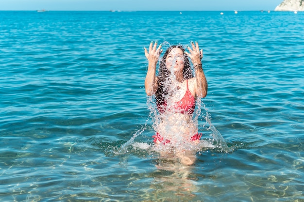 Ragazza che si diverte mentre fa il bagno in mare e spruzza acqua