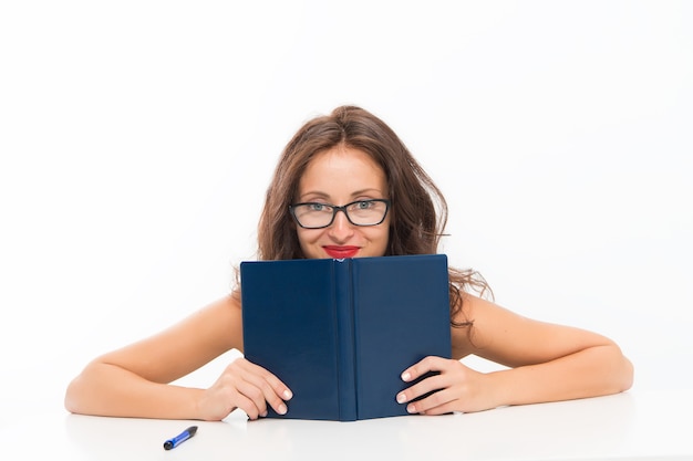 Ragazza che si nasconde dietro un libro che guarda la telecamera flirta e desidera una ragazza che legge un libro con gli occhiali Introverso