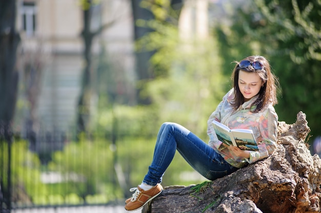 Ragazza che si siede nel parco e che legge un libro