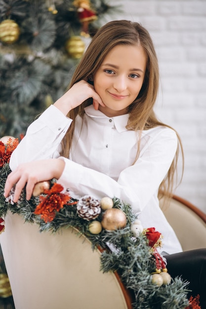 Ragazza che si siede nella sedia in studio con decorazione di Natale