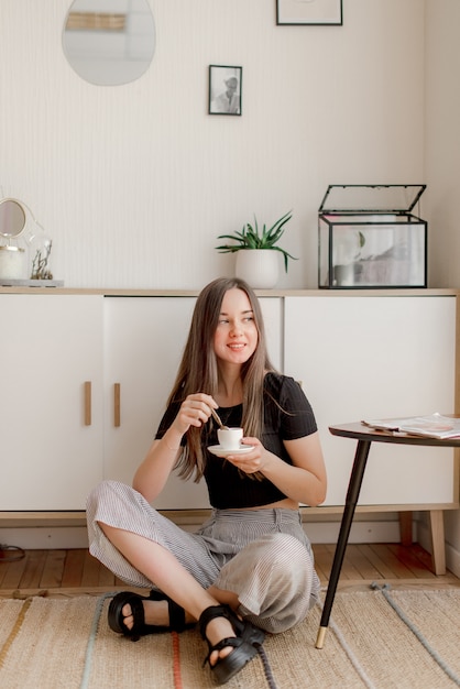 Ragazza che si siede su un pavimento con la tazza di caffè