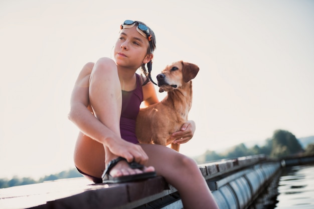 Ragazza che si siede sul bacino del fiume con il suo cane