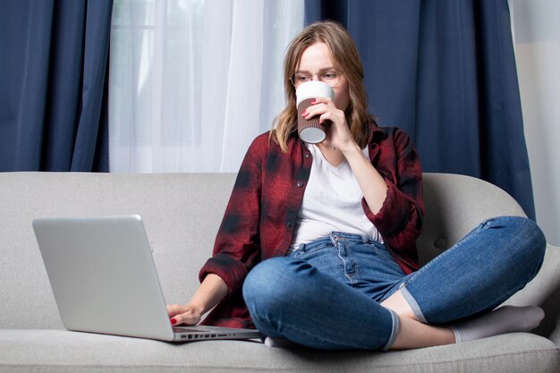 Ragazza che si siede sul divano con un computer portatile