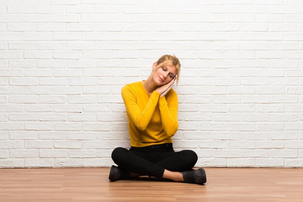 Ragazza che si siede sul pavimento che fa gesto di sonno nell&#39;espressione dorable