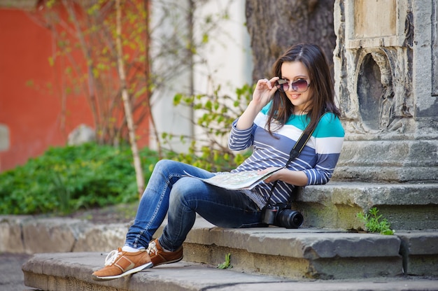 Ragazza che si siede sulle scale con una macchina fotografica e una mappa in mano