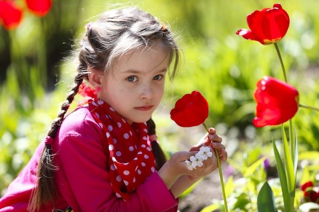 Ragazza che si siede vicino ai tulipani rossi. Annusa i fiori