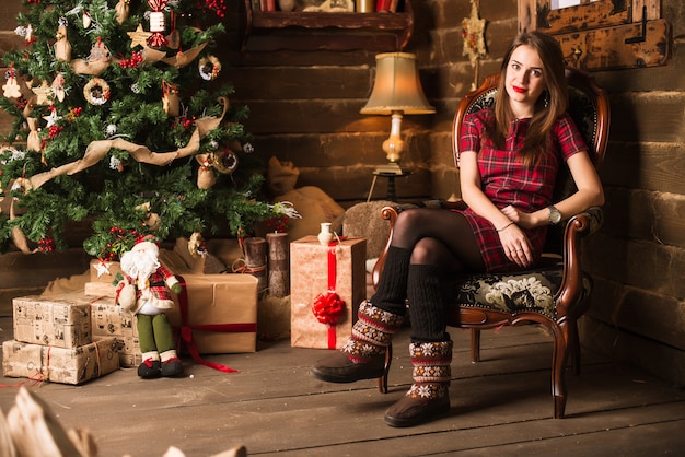 Ragazza che si siede vicino all'albero di Natale e ai regali