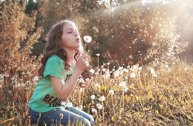 Ragazza che soffia i semi da un fiore di dente di leone nel pomeriggio autunnale