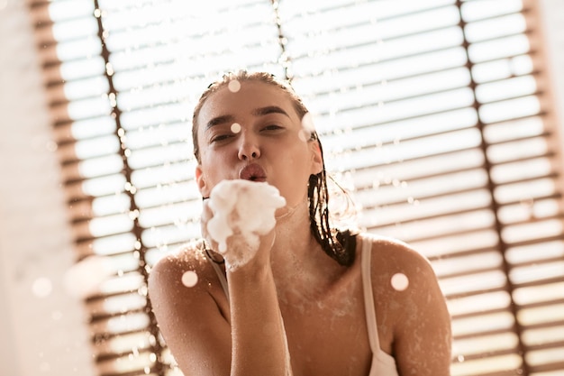 Ragazza che soffia le bolle di sapone facendo la doccia a casa