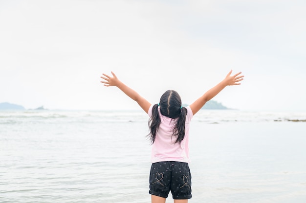 Ragazza che solleva le mani sulla spiaggia, libertà