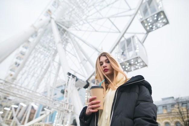 Ragazza che sta in un parco con caffè in sue mani