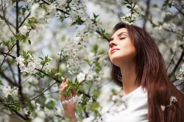 Ragazza che sta sotto di melo sbocciante in parco naturale.