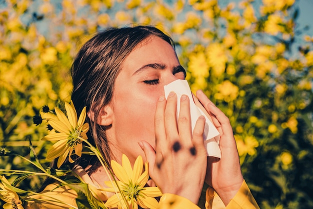 Ragazza che starnutisce e tiene in una mano il fazzoletto di carta e nell'altra il bouquet di fiori. Giovane donna