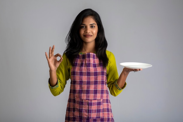 Ragazza che tiene e che posa con il piatto e la ciotola degli utensili da cucina su un gray