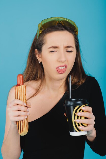 ragazza che tiene hot dog e vetro con caffè su sfondo blu