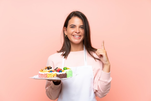 Ragazza che tiene i lotti di mini torte differenti sopra la parete isolata che indica su una grande idea