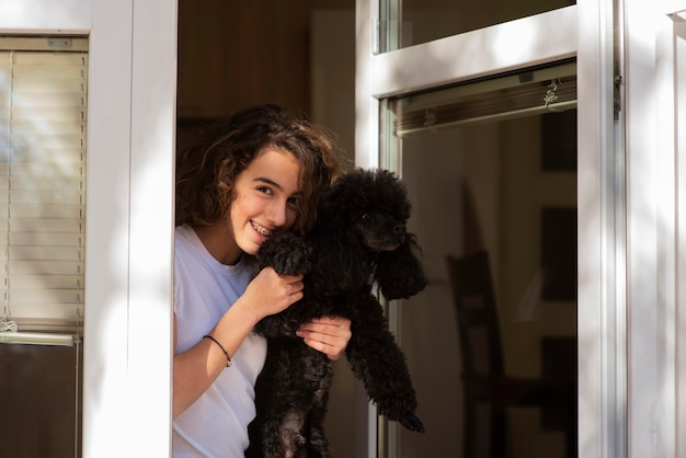 Ragazza che tiene il suo cane durante il soggiorno con una finestra aperta