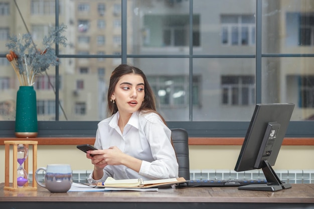 Ragazza che tiene il telefono con entrambe le mani e guarda il pc