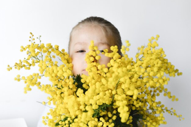 Ragazza che tiene la mimosa su uno sfondo bianco della parete