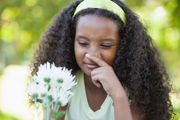 Ragazza che tiene un fiore e che copre il suo naso nel parco