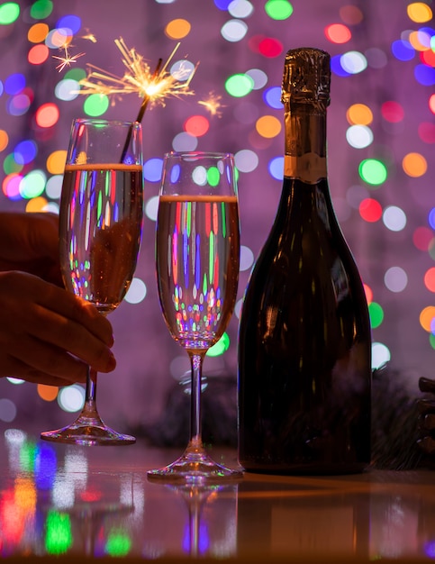 Ragazza che tiene un fuoco bengalese e un bicchiere di champagne su un bellissimo bokeh festivo luci