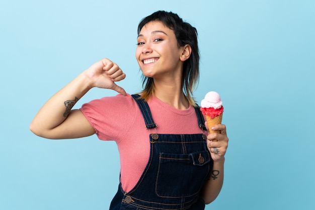 Ragazza che tiene un gelato della cornetta sopra la parete blu fiera e soddisfatta di sé