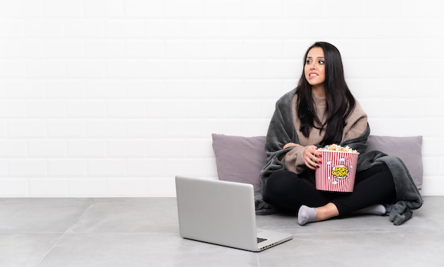 Ragazza che tiene una ciotola di popcorn e che mostra un film in un computer portatile con l'espressione confusa del fronte