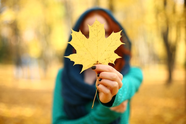 Ragazza che tiene una foglia d'acero gialla in autunno =