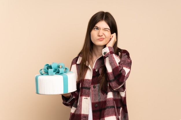 Ragazza che tiene una grande torta isolata sulle orecchie frustrate e coprenti beige