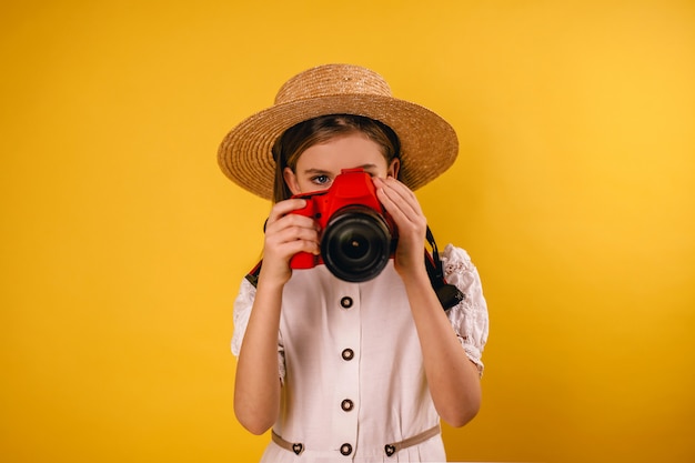 Ragazza che tiene una macchina fotografica in sue mani su una priorità bassa gialla e che cattura le immagini