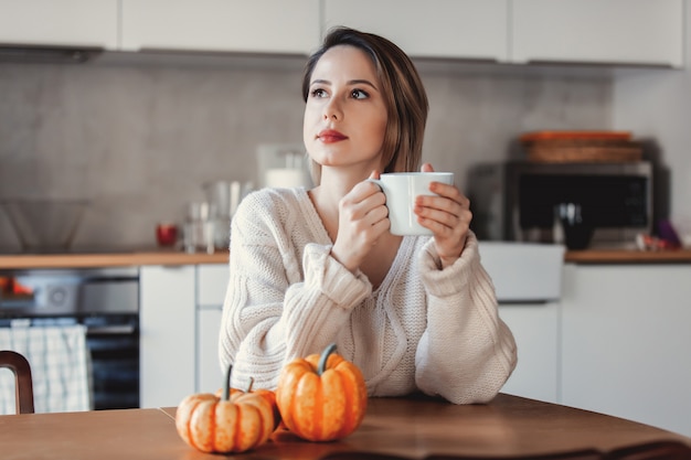 Ragazza che tiene una tazza di caffè e che si siede alla tavola