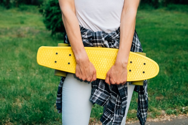 Ragazza che tiene uno skateboard di plastica gialla nel parco