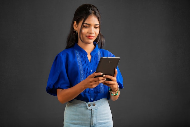 Ragazza che utilizza il telefono cellulare o lo smartphone su sfondo grigio